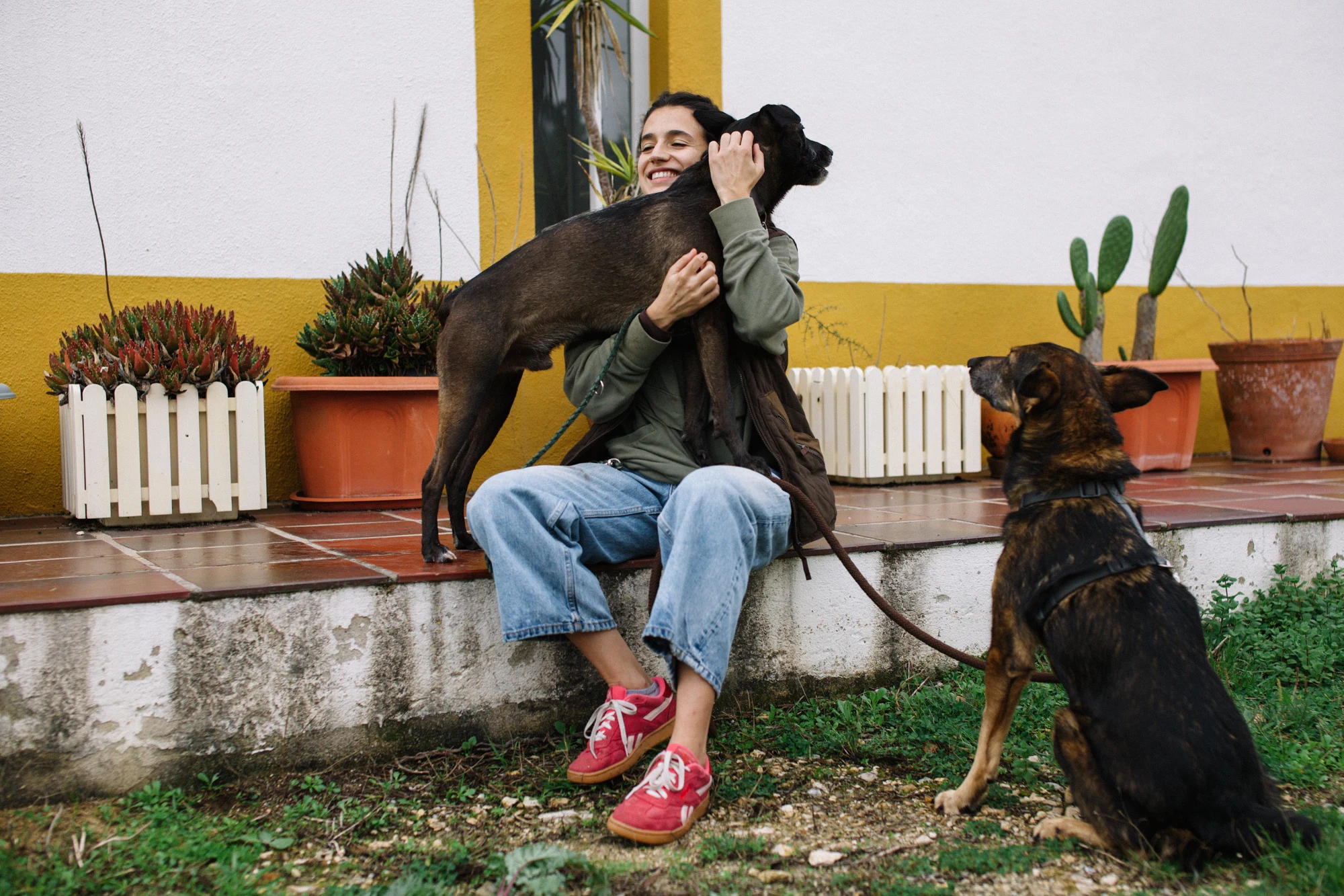 Uma tutora abraça um cão, com outro cão ao seu lado